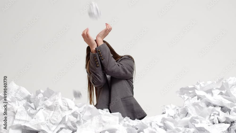 Female office worker stands waist-deep in pile of crumpled papers and closes hands from crumpled lumps of documents flying into her, front view