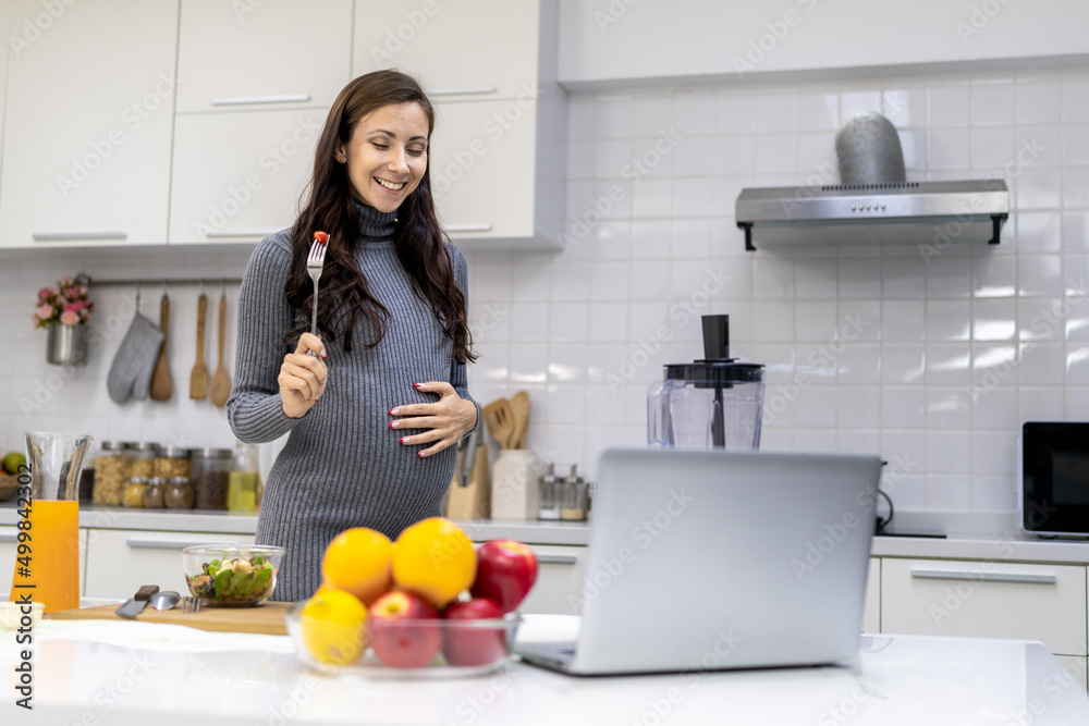 Healthy and cheerful pregnant woman preparing food for herself in her home kitchen. The menu is a vegetable and fruit salad. Healthy and cheerful pregnant woman preparing food for herself in her home kitchen. The menu is a vegetable and fruit salad.