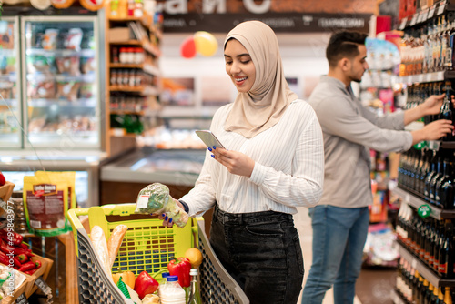 Middle Eastern Lady Buyer Shopping Using Cellphone In Supermarket