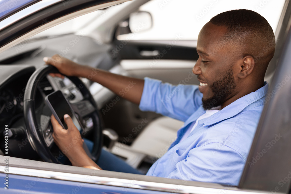 Happy black man using showing smartphone driving car