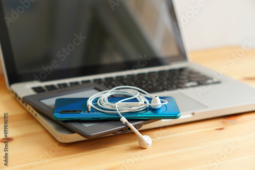 Smartphone and e-books, tablet and earphones on the laptop computer, electronic gadgets for daily use on wooden background.