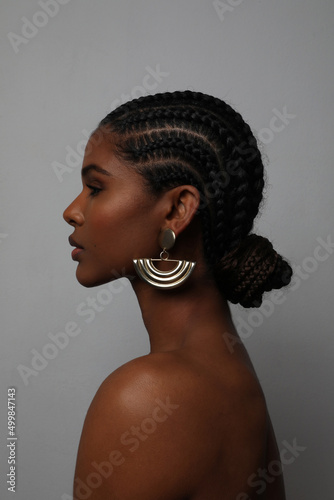 Side profile portrait of African young woman with braids posing on grey wall.