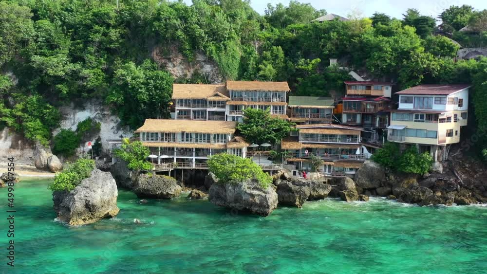aerial drone panning across a hotel and houses on a cliff in Uluwatu Bali with an Indonesian flag waving over the tropical turquoise blue ocean on a sunny day aerial drone panning across a hotel and houses on a cliff in Uluwatu Bali with an Indonesian flag waving over the tropical turquoise blue ocean on a sunny day