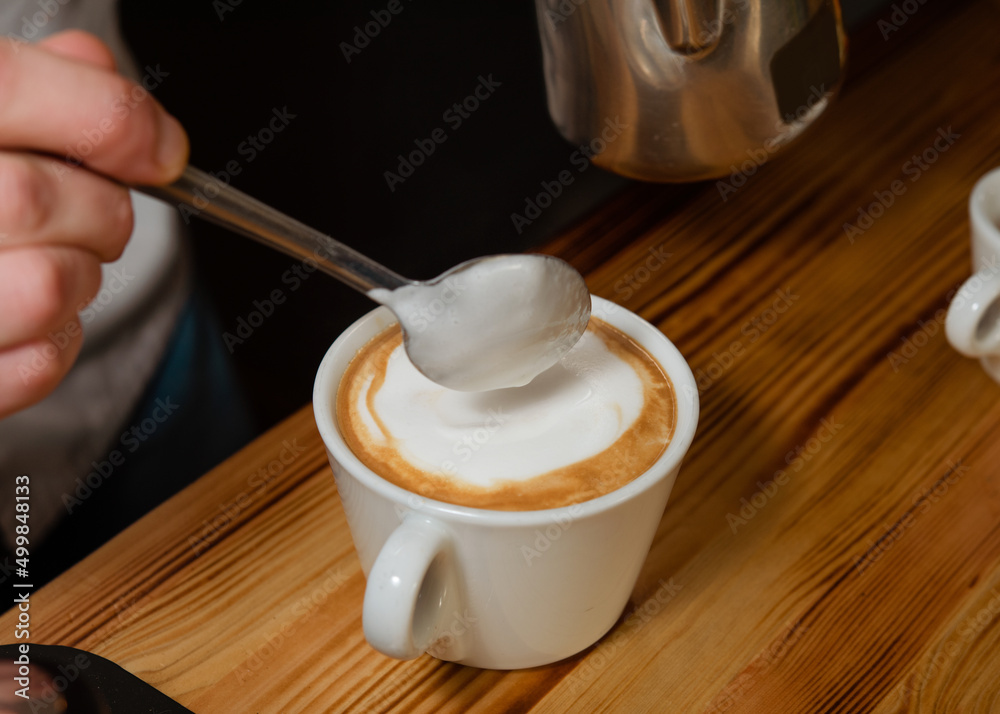the barista holding a spoon in  hand and pouring milk into a cup of coffee