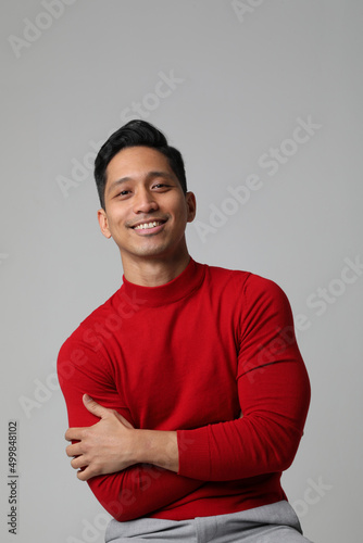 Vertical portrait of smiling Asian businessman standing near white wall. 