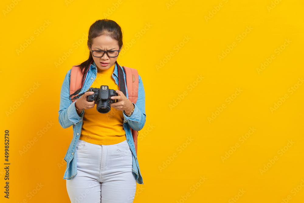 Portrait of surprised young Asian woman looking at photo on camera isolated on yellow background. Passenger traveling on weekends. Air flight journey concept