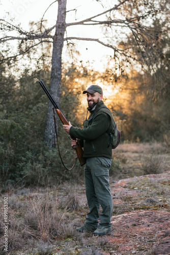Man looking at camera and smiling while holding shotgun during hunting.