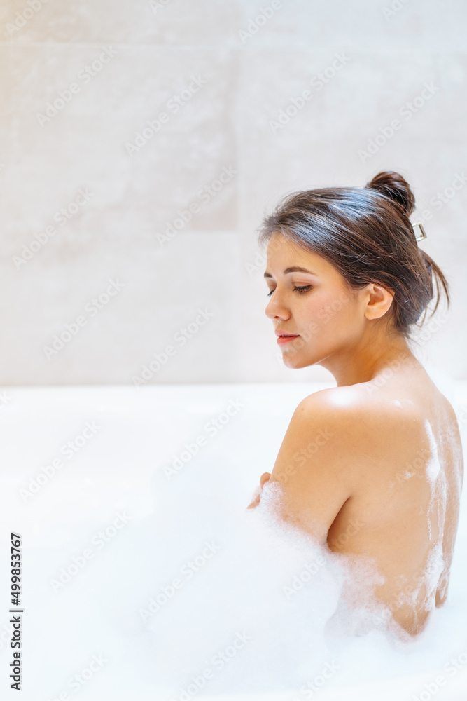 Young bare woman sitting in white bubble bathtub, free copy space. Young bare woman sitting in white bubble bathtub, free copy space.
