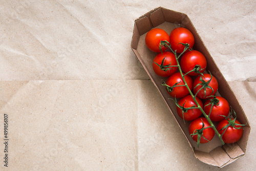 Fresh red cherry tomatoes on a branch, in organic packaging on a beige background, top view. Copy space.