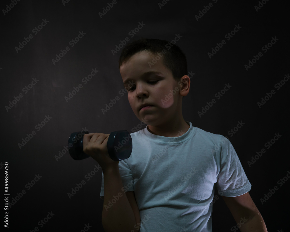 A boy on a black background with dumbbells.A sporty boy.lifts a dumbbell with one hand A boy on a black background with dumbbells.A sporty boy.lifts a dumbbell with one hand