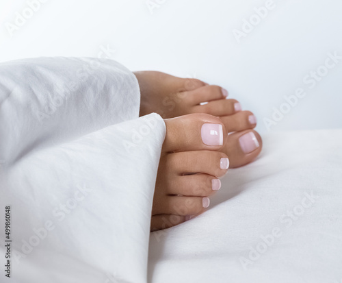 Female feet with french pedicure under white blanket. Care concept. Beauty saloon