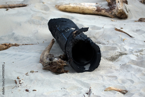 Fototapeta Naklejka Na Ścianę i Meble -  Zanieczyszczona plaża wyrzucone na brzeg odpady plastikowe duża gumowa rura plastikowy przewód	
