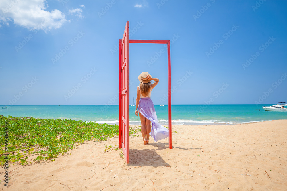 Tropical travel vacation. Traveler woman walks out in red door on the sandy beach to turquoise sea, toward vacation and relaxation in sunny Asia. Carefree girl tourist in swimwear in Asian destination Tropical travel vacation. Traveler woman walks out in red door on the sandy beach to turquoise sea, toward vacation and relaxation in sunny Asia. Carefree girl tourist in swimwear in Asian destination