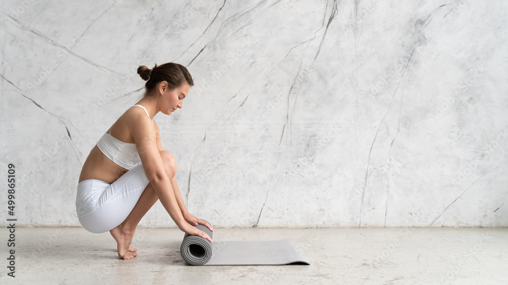 Banner of woman rolling her mat with both hands on after yoga class with copy space on the wall