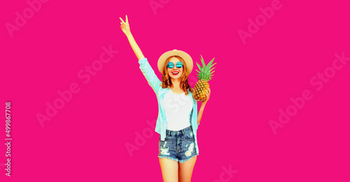 Summer vacation  happy laughing woman raising her hands up with pineapple having fun wearing straw hat on pink background