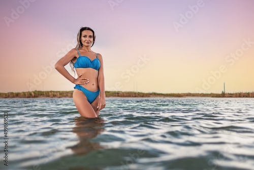 Girl with blond hair in a swimsuit posing against the backdrop of the sunset in the estuary enjoying nature around him