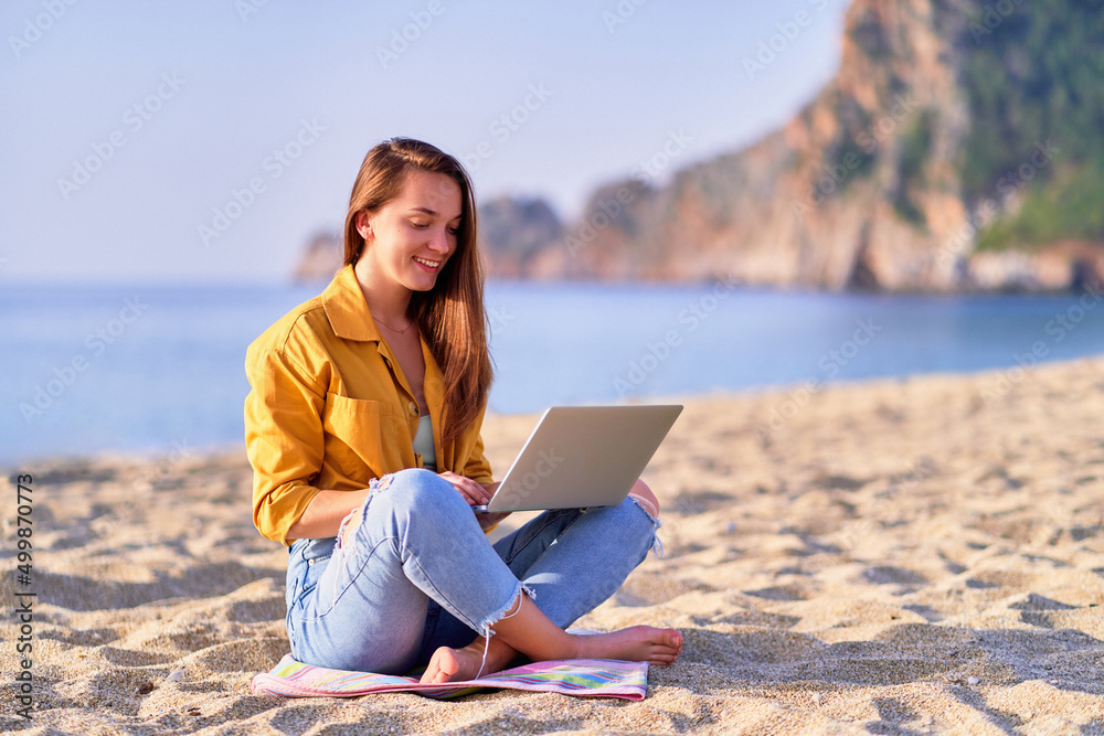 Young happy joyful satisfied millennial freelancer girl using laptop on the beach by sea. Dream office work concept