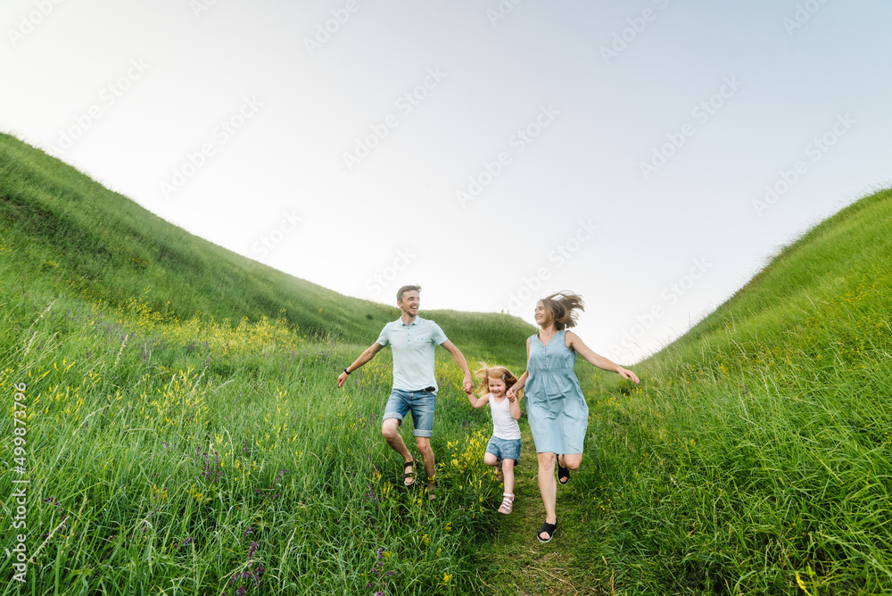 Mom, dad and daughter walk in the green grass. Happy young family spending time together, running outdoors. The concept of family holiday. Mom, dad and daughter walk in the green grass. Happy young family spending time together, running outdoors. The concept of family holiday.