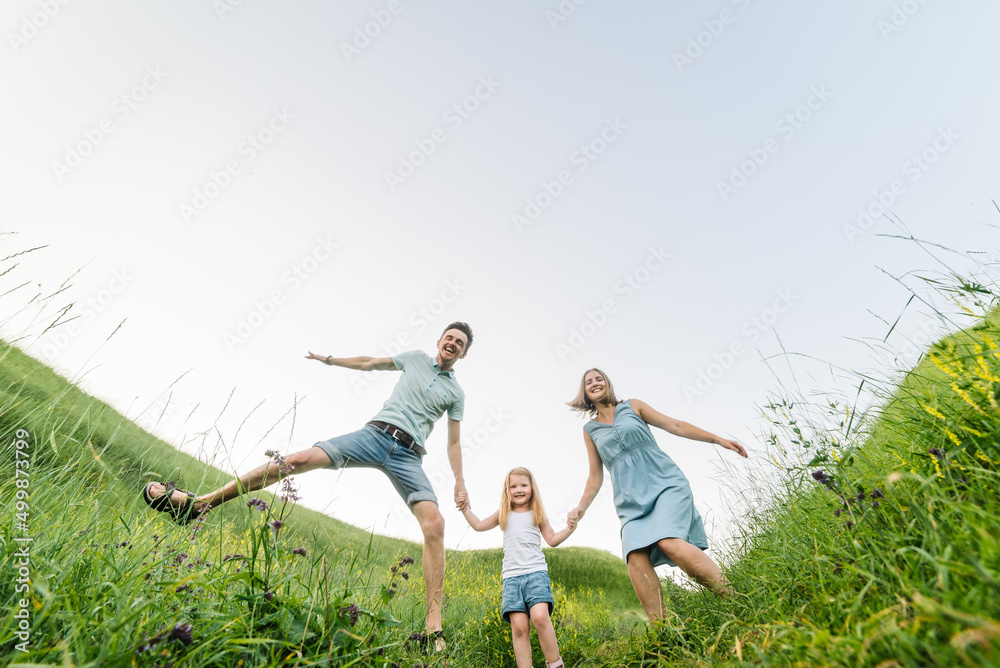 Happy family in the park. Parents hold the child's hands. Mom, dad, and daughter walk in the field. The concept of a family holiday.