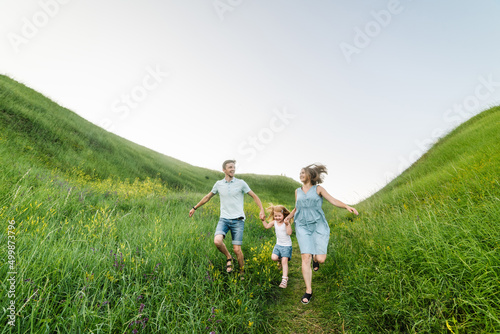 Mom, dad and daughter walk in the green grass. Happy young family spending time together, running outdoors. The concept of family holiday.