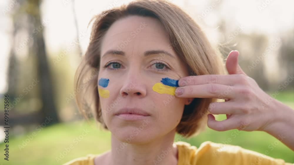 Patriot woman draws flag of Ukraine on her face. Close-up. Portrait of serious middle-aged female Ukrainian patriot. Patriot woman draws flag of Ukraine on her face. Close-up. Portrait of serious middle-aged female Ukrainian patriot.