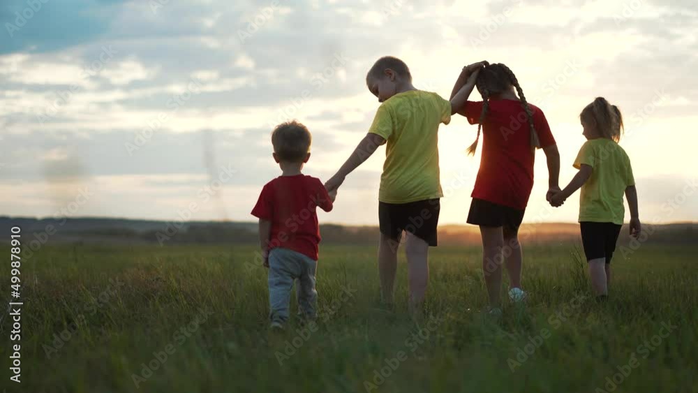 Happy family. Children holding hands walk on green grass. Happy children play at sunset in the park. Cheerful children walk in the field. Active lifestyle. Family picnic on green grass. Dream concept Happy family. Children holding hands walk on green grass. Happy children play at sunset in the park. Cheerful children walk in the field. Active lifestyle. Family picnic on green grass. Dream concept