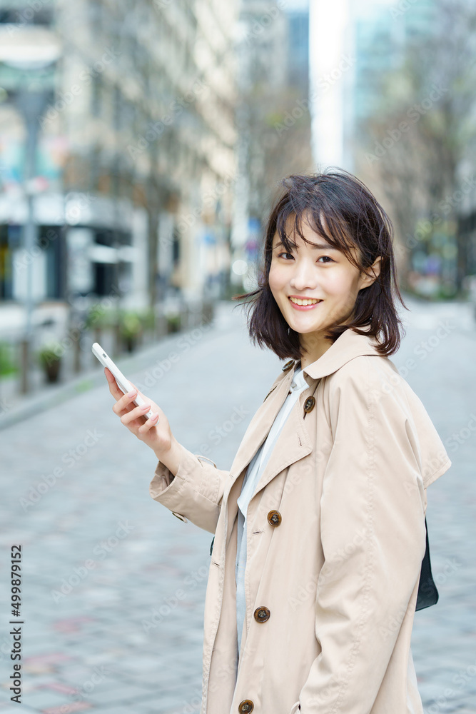 スマートフォンを手にビジネス街を歩く女性 スマートフォンを手にビジネス街を歩く女性