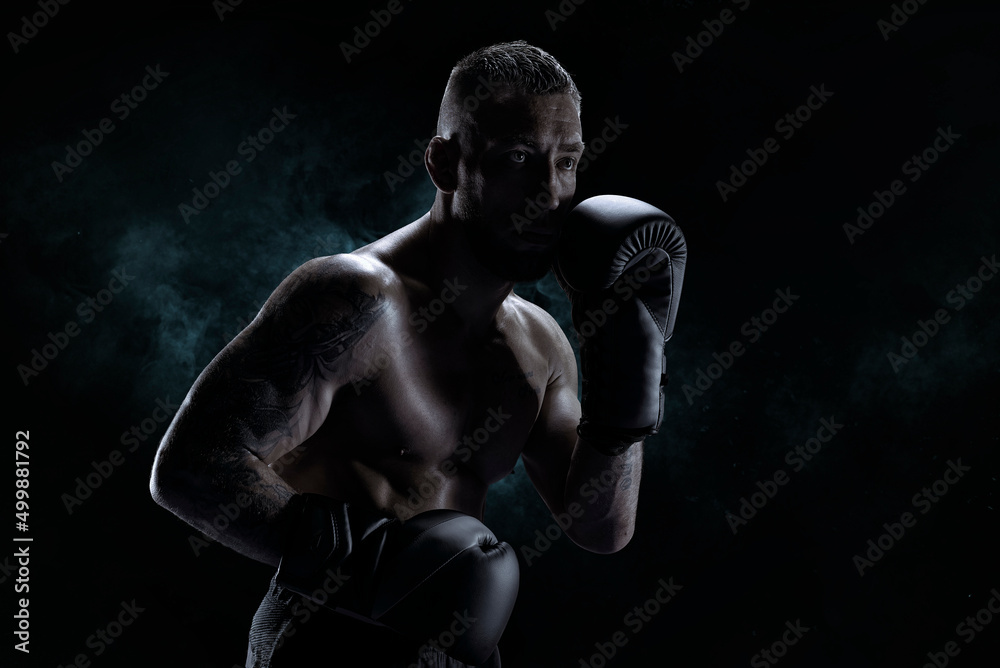 Kickboxer in black gloves posing on a background of smoke. The concept of mixed martial arts.