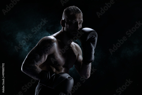 Kickboxer in black gloves posing on a background of smoke. The concept of mixed martial arts. © andy_gin