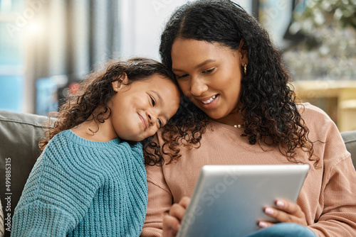 This looks nice, dont you think. Shot of an attractive young woman sitting and bonding with her daughter while using a digital tablet.