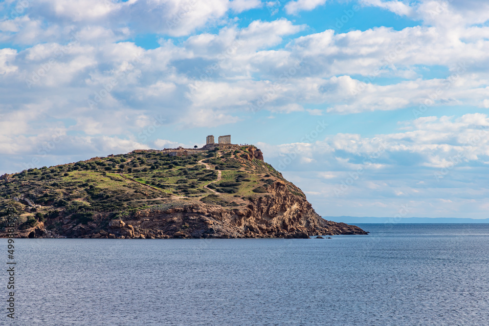 The Temple of Poseidon on a rock rises above the blue sea. Beautiful seascape. Europe, Greece, Cape Sounion, Aegean Sea