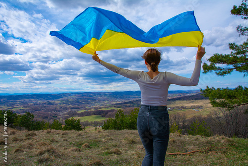 A young woman with a flag of Ukraine against the background of beautiful view to mountains