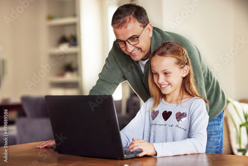 Dad, come and see this. Shot of an adorable little girl sitting and using a laptop at home while her father helps her. © Alexis Scholtz/peopleimages.com