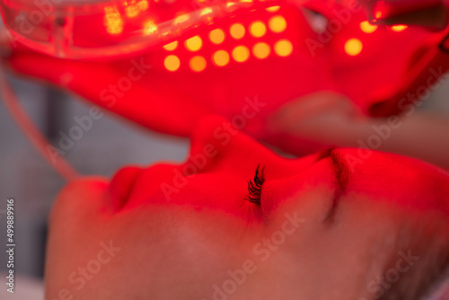 LED light anti-aging mask for facial skin care in a spa slow motion. A woman lies on a couch in a special mask. Modern technologies of beauty and health. photo