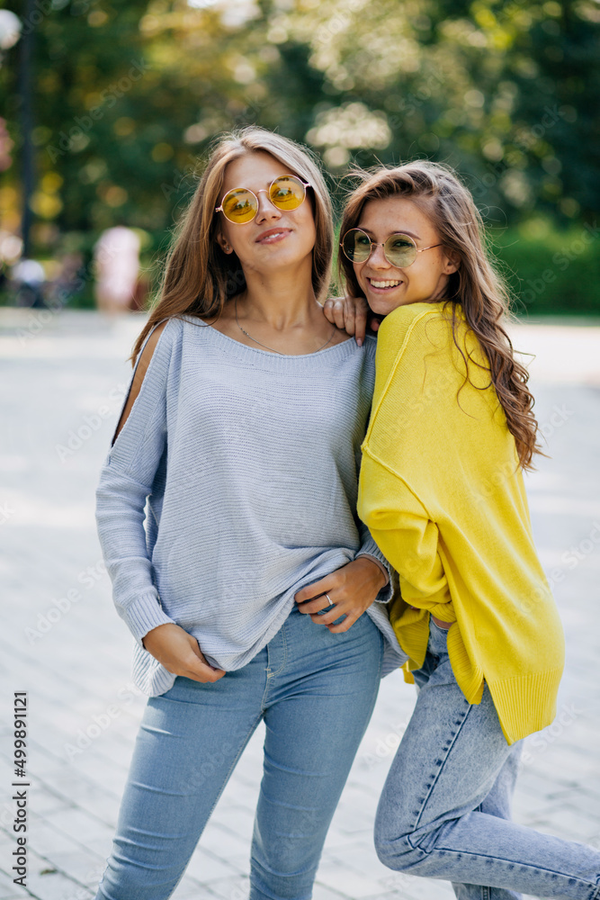 Fototapeta premium Close-up portrait of positive two stylish girls hugging on street in city. Closeup portrait of lovely joyful attarctive young women having fun, smiling, lovely moments, best friends