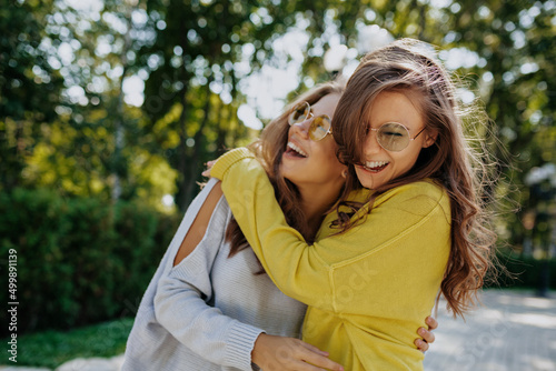 Emotional two adorable girls are hugging and smiling while spending time outside in warm summer day