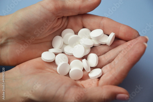 A handful of white round pills in the palms on a blue background. The concept of health and medicine, treatment, pharmaceuticals.
