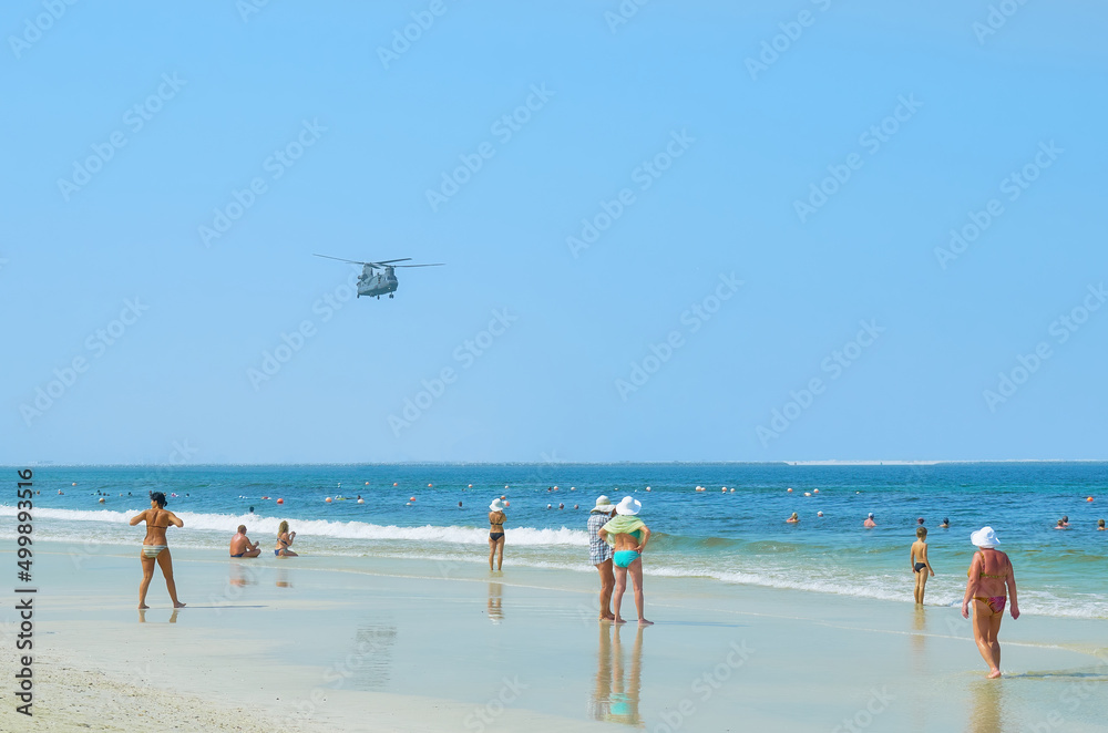 Sharjah, UAE - 12 October, 2017. A military helicopter flies over a crowded beach. Rest on the sea. Sharjah, UAE - 12 October, 2017. A military helicopter flies over a crowded beach. Rest on the sea.