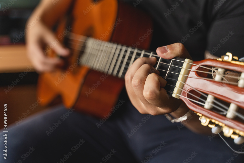 A young guy is playing a classical guitar in his room during the day