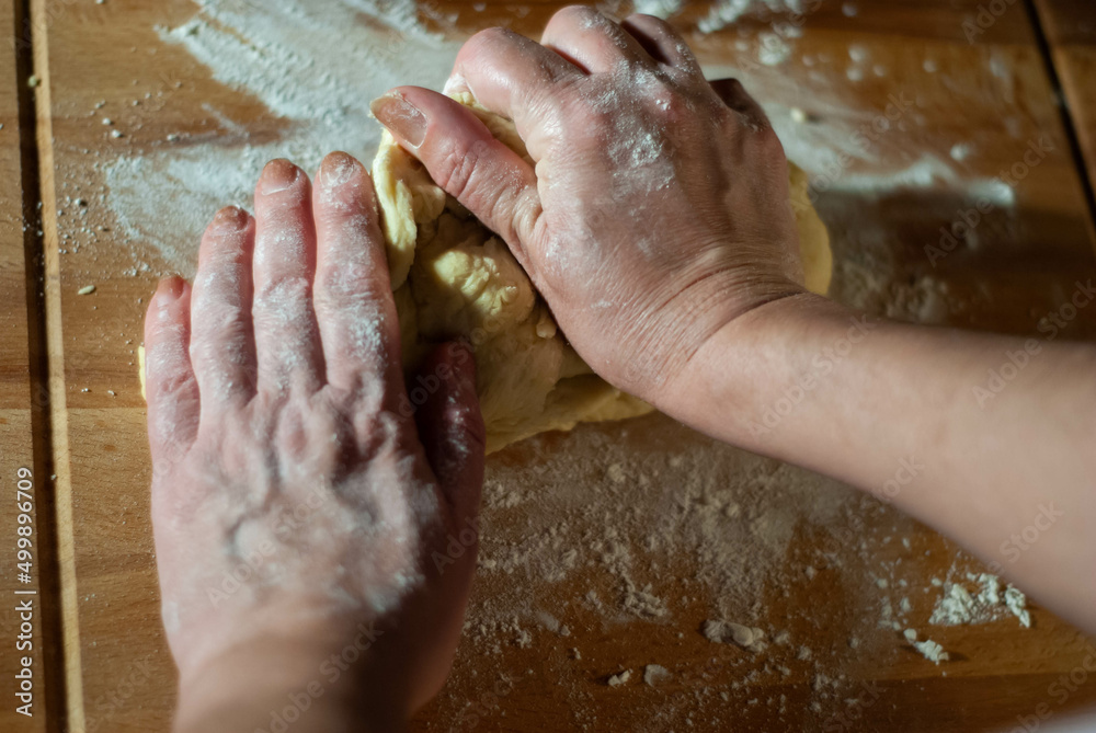 Fototapeta premium Baker's hands working the flour dough on a wooden board