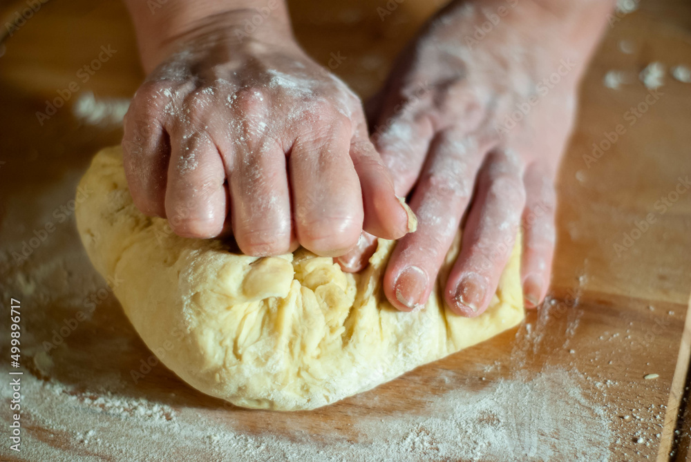 Baker's hands working the flour dough on a wooden board