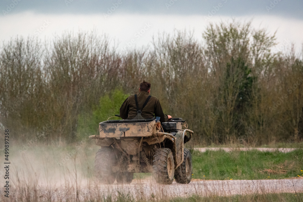 Obraz premium a farmer quad biker throws up clouds of dust riding his off-road quad bike along a stone track open countryside