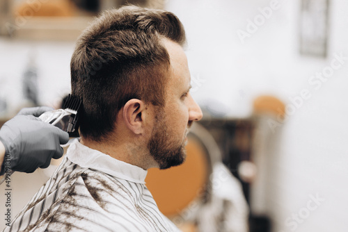 Young handsome barber making haircut of attractive man in barbershop