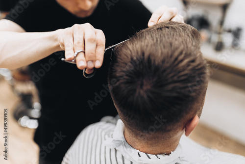 handsome young bearded guy sitting in an armchair in a beauty salon and the barber near him cuts his hair