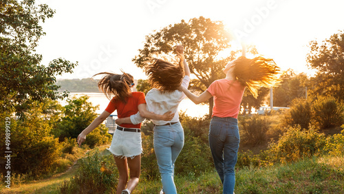 Group of girl friends jumping outdoors on sunset nature. Young multi-ethnic hipster friends dancing at summer party. Group of women friends hugging and ejoying the sunset in outdoor nature photo