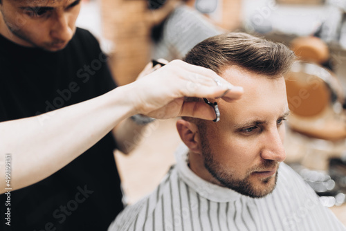 handsome young bearded guy sitting in an armchair in a beauty salon and the barber near him cuts his hair