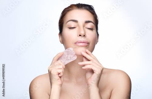 Woman doing Gua Sha. Beautiful woman enjoying a beauty face treatment with a quartz pink guasha. Chinese traditional massage