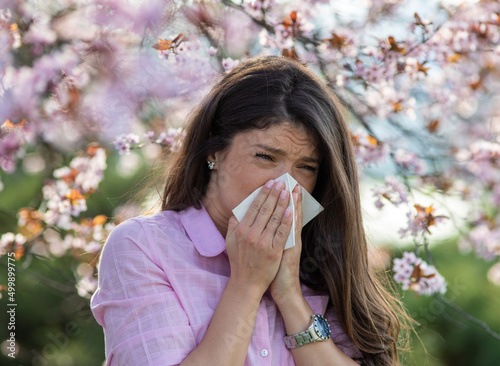 Girl wiping nose in front of blooming tree in spring
