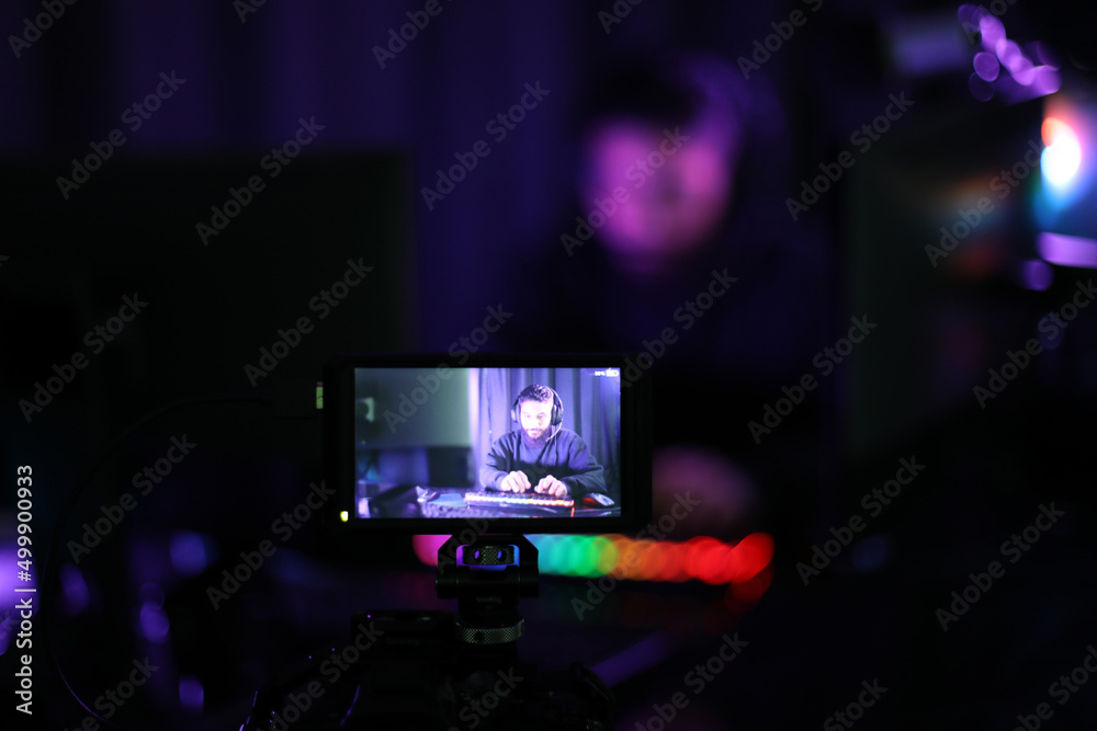 Fototapeta premium personal view photos through the screen Live show boys playing online games in headphones, keyboards are brightly colored. In a dark room with colorful neon lights