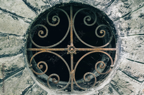 Ancient wrought iron lattice of a round basement window. Wrought iron pattern.